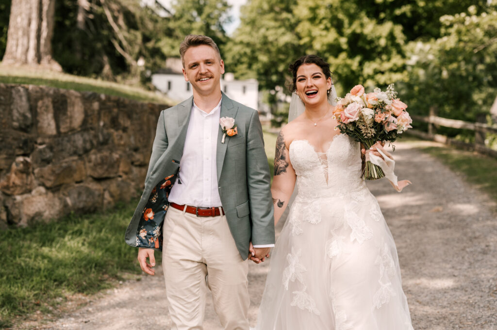 The couple holding hands and laughing as they walk down a rocky path at Waterloo Village.