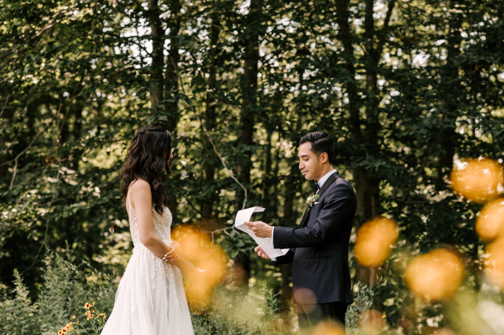 The groom reading a letter to the bride surrounded by greenery at Rock Island Lake Club.