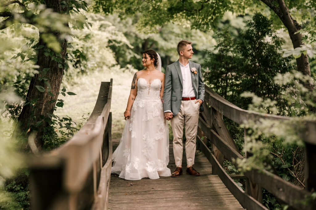 The bride and groom holding hands as they look in opposite directions on a bridge at Waterloo Village.
