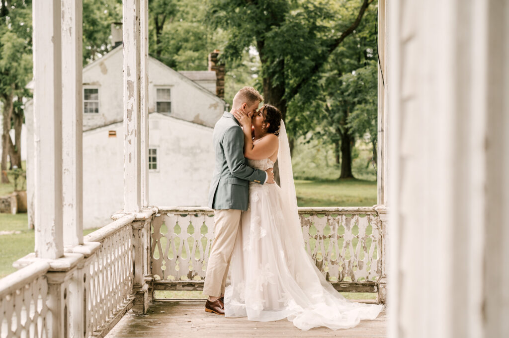The bride and groom sharing a kiss as they embrace on a porch at Waterloo Village.