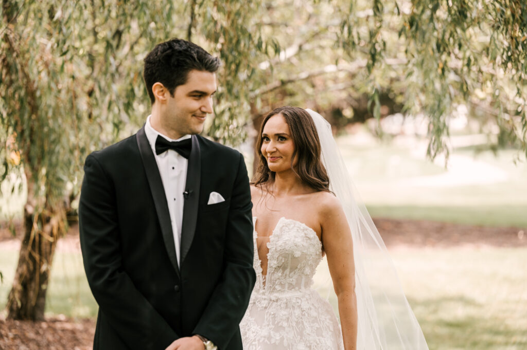 The bride tapping on the groom's shoulder to signal him to turn around for their first look at Perona Farms Refinery.