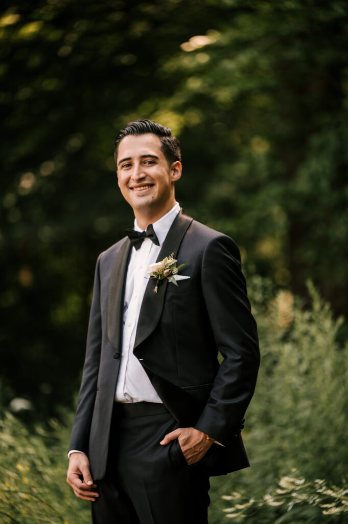 The groom posing and smiling with a hand in his pocket.