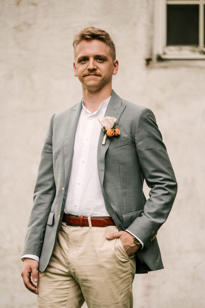 The groom smiling and posing with his hand in his pocket as he walks.