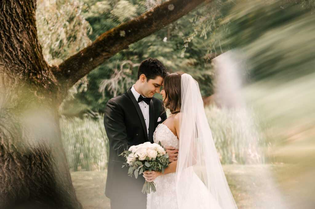 The bride and groom touching foreheads in an embrace under a tree at Perona Farms Refinery.