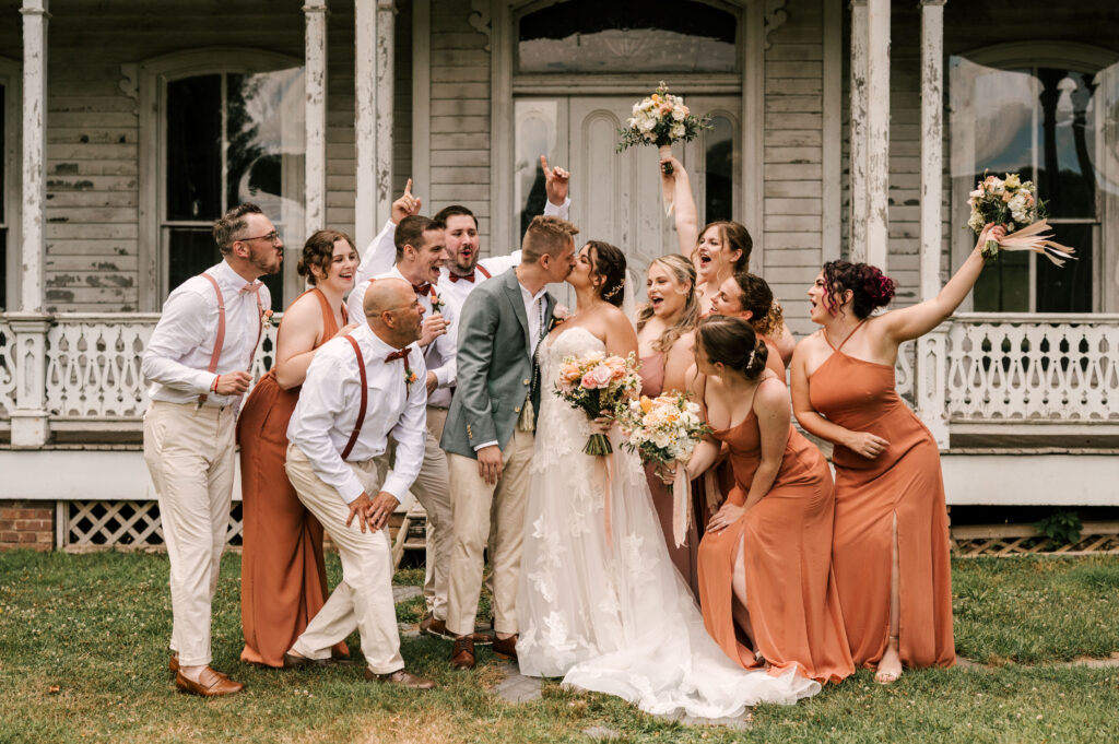 The bridesmaids and groomsmen cheering as the bride and groom share a kiss at Waterloo Village.