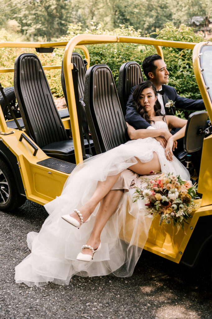 The groom in the driver's seat of a Moke with his arm around the bride in the passenger seat as she leans back onto him at Rock Island Lake Club.