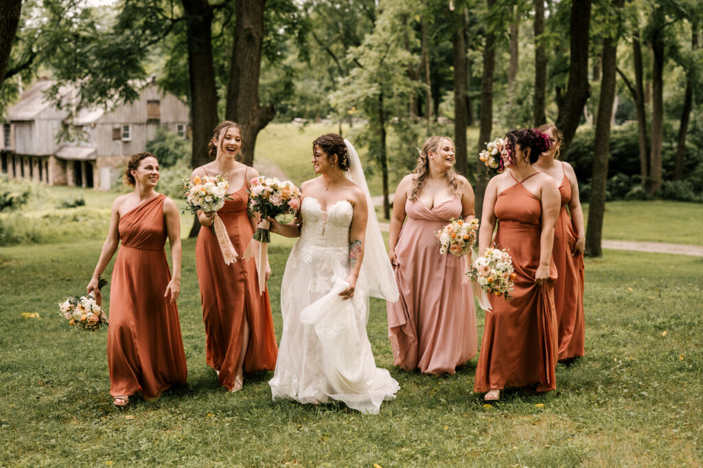 The bride and her bridesmaids talking and giggling as they walk through the grass at Waterloo Village.