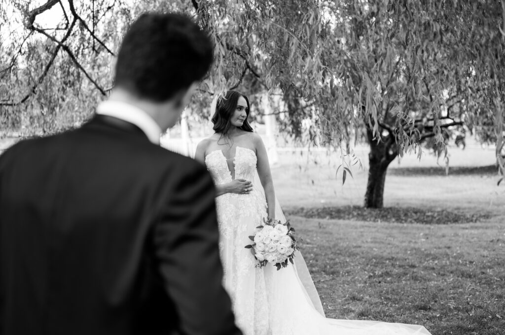 The groom looking at the bride as she stands under a tree at Perona Farms Refinery.