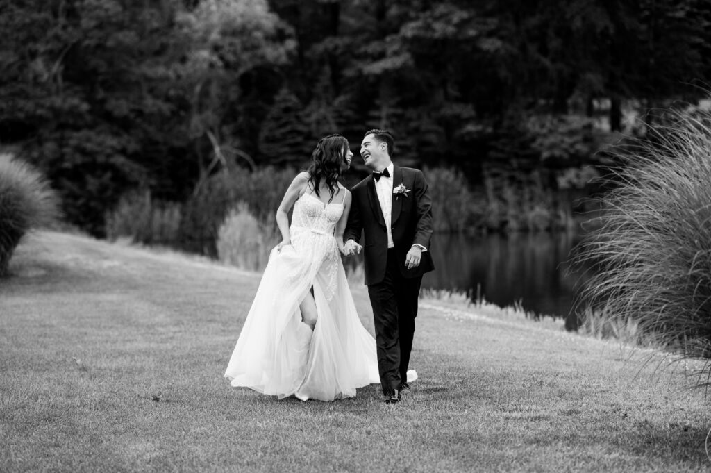 The couple holding hands walking through a field as they smile and lean into each other at Rock Island Lake Club.