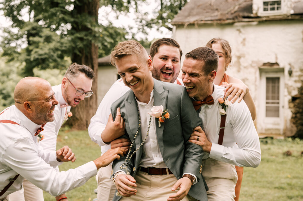 The groomsmen playing around with the groom as they smile and laugh at Waterloo Village.