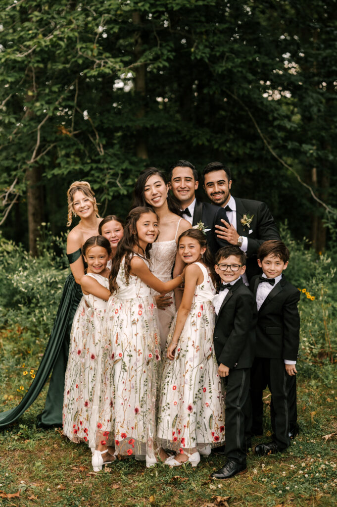 The bride and groom smiling and posing with their maid of honor, best man, and flower girls.