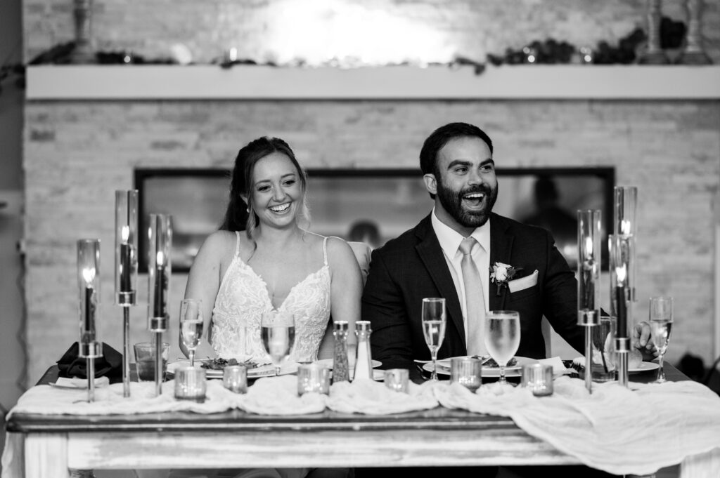 The couple laughing at the sweetheart table during the reception.