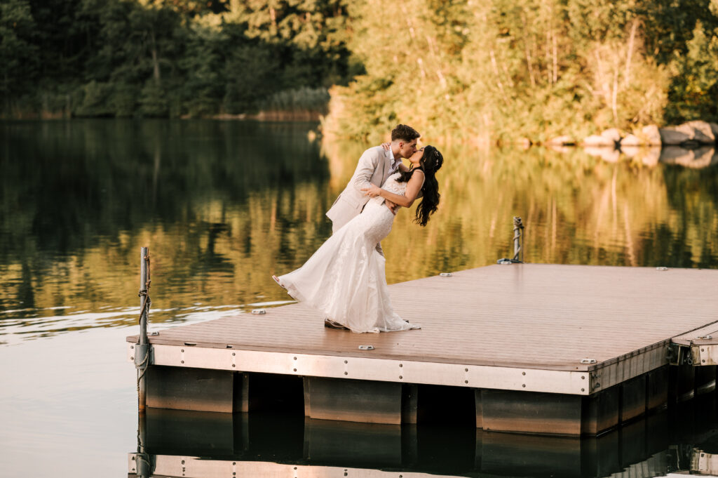 Bride and groom dip kissing at sunset on the dock overlooking the lake at Rock Island Lake Club