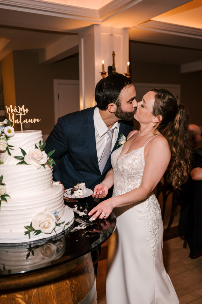 The bride and groom sharing a kiss as they cut their wedding cake at their reception at Rock Island Lake Club.
