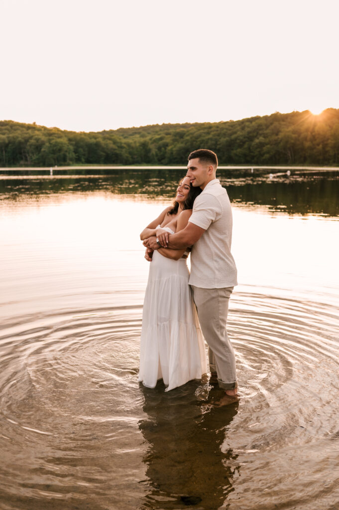 The newly engaged coupl smiling and embracing during golden hour on the lake at Wawayanda State Park.
