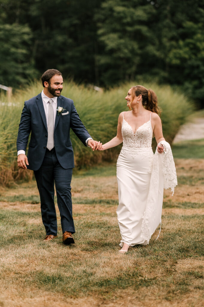 The couple holding hands and walking through the grass and foliage at Rock Island Lake Club.