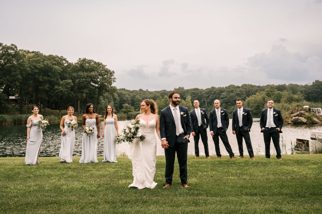 The bride and groom holding hands as the bridal party stands behind them at Rock Island Lake Club.