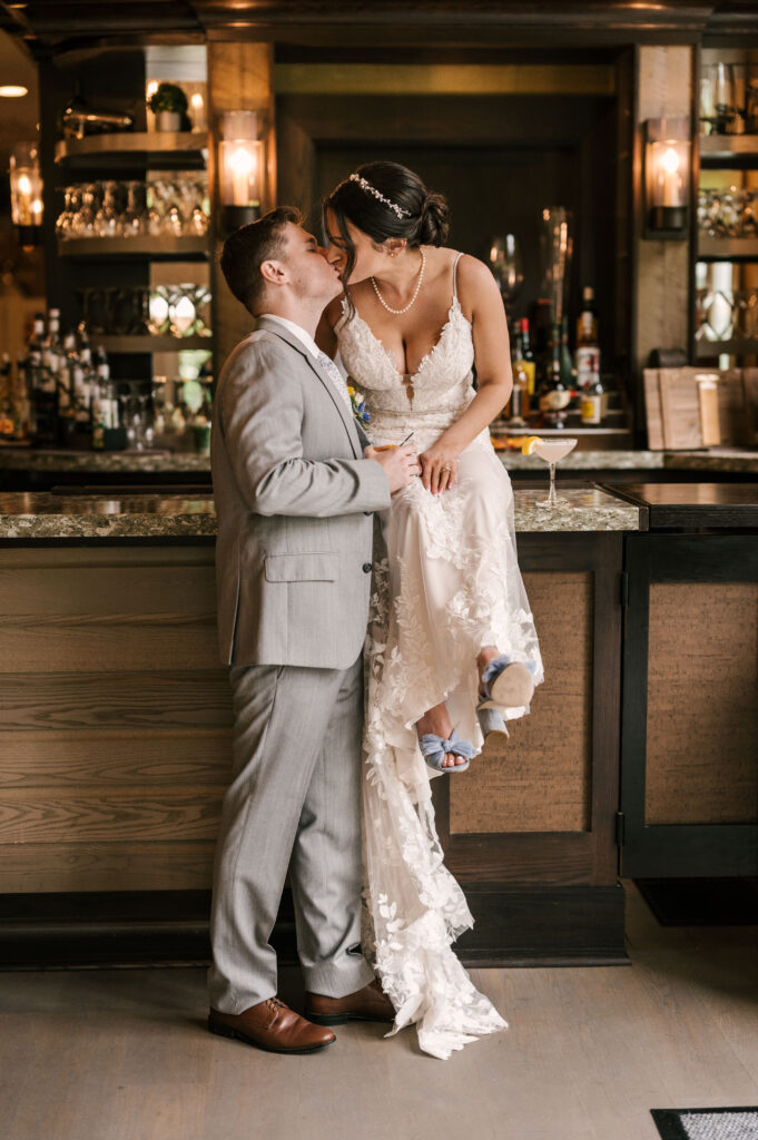 Bride and groom sit at the bar and kiss at their indian trail club wedding in Franklin Lakes NJ