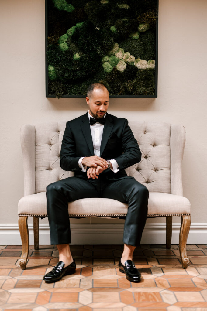 The groom sitting on a chair, checking his watch at Perona Farms Reserve.