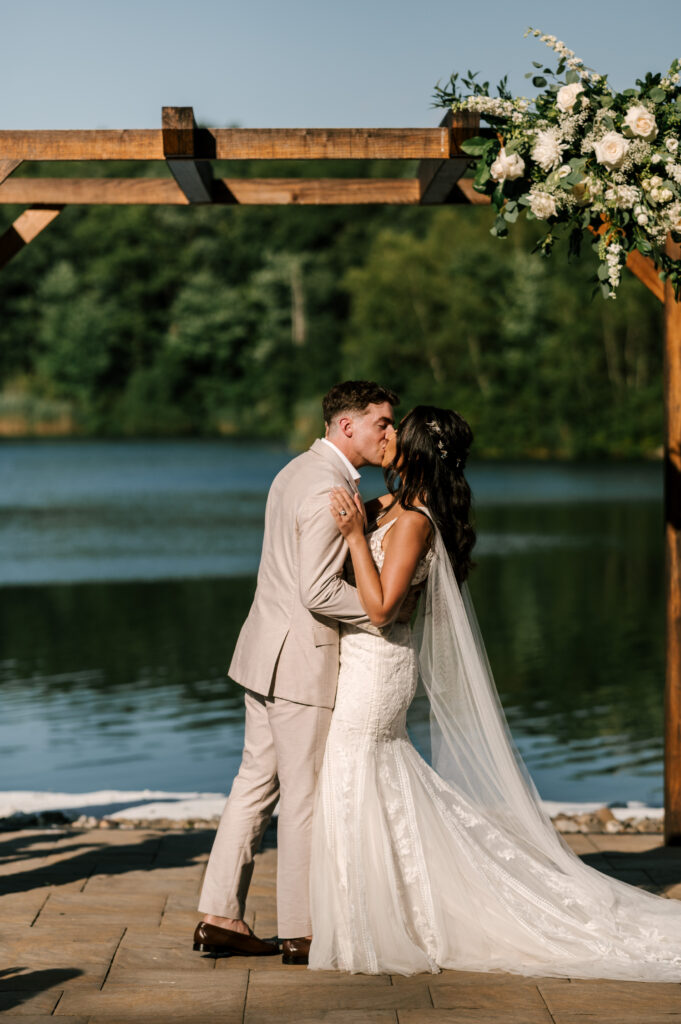 bride and groom sharing first kiss in front of lake at rock island lake club wedding in nj 