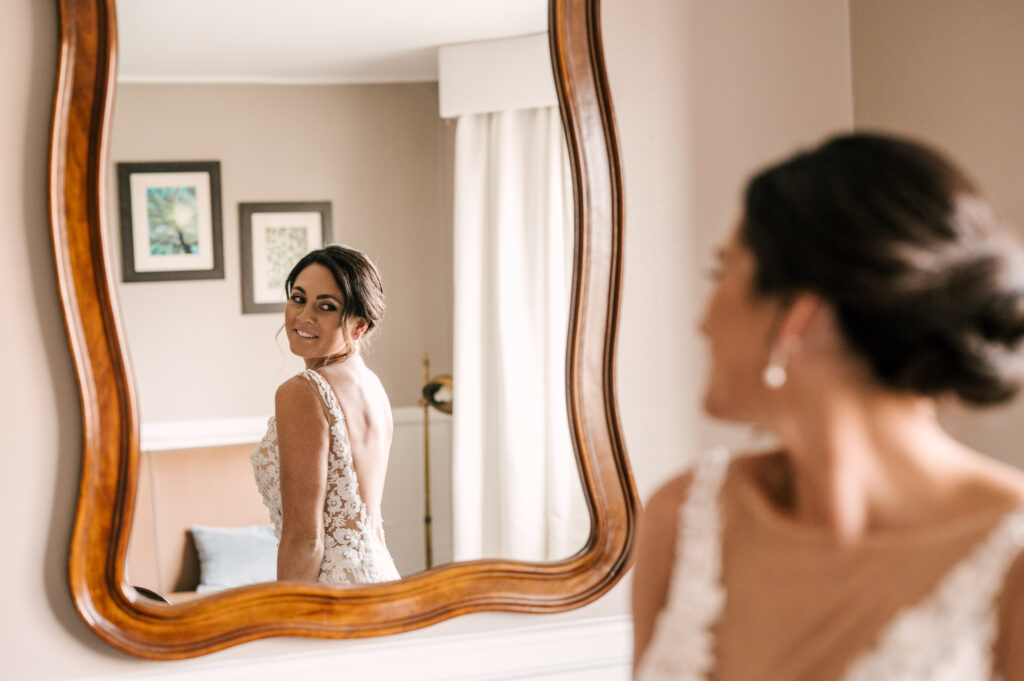 bride looking at herself in mirror while putting wedding dress on at september wedding in new york