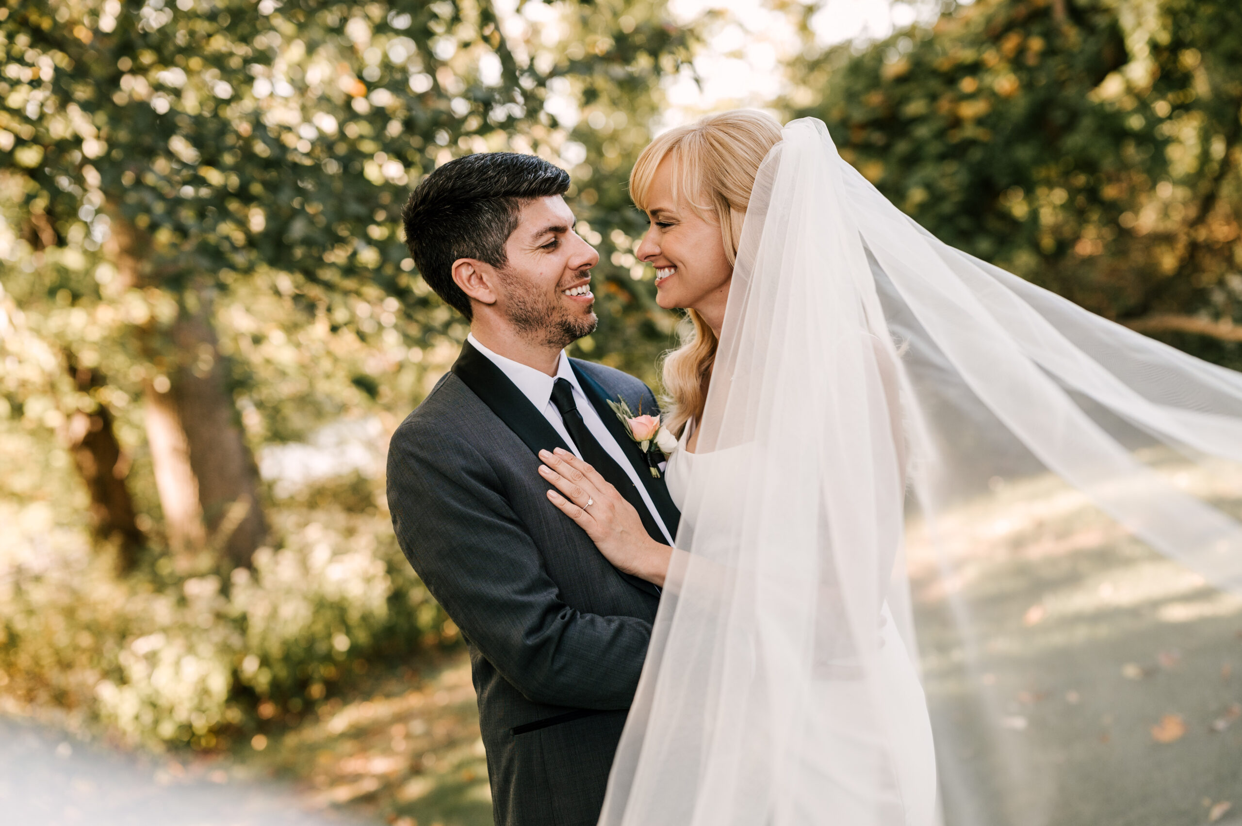 bride and groom smiling at one another with bride's veil flowing