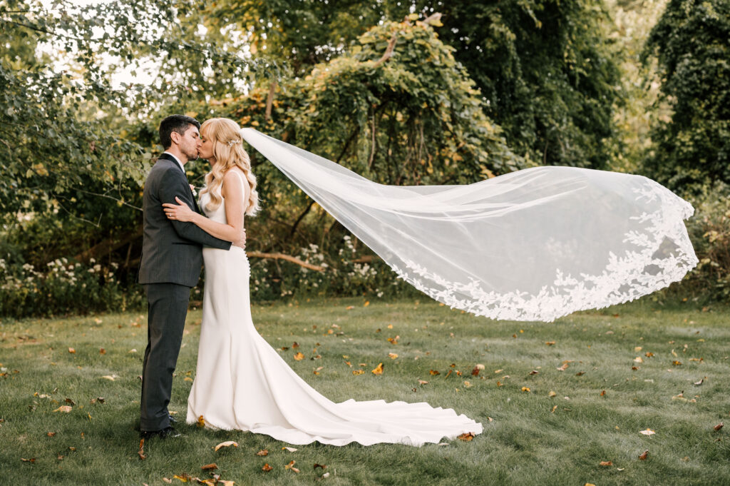 bride and groom with bride's veil floating behind her in a lush greenery area at perona farms in nj 