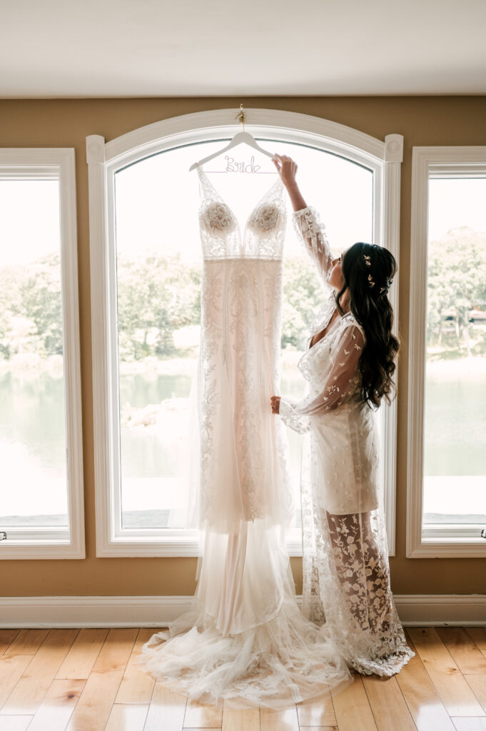 august wedding in nj, bride holding up wedding dress in front of large window at rock island lake club