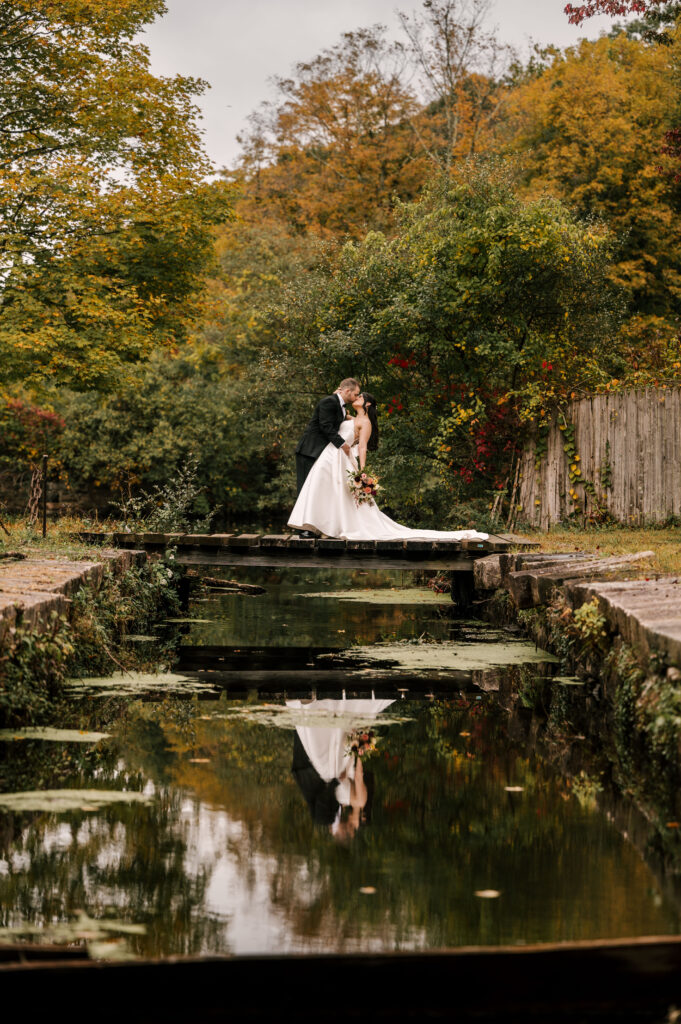 bride and groom kissing on a wooden bridge at waterloo village with reflection seen in water