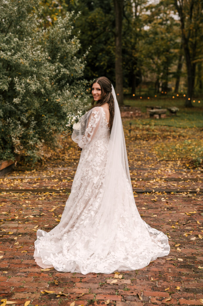 bride in her long sleeve lace wedding gown looking back at camera with fairy lights in background at waterloo village nj wedding venue