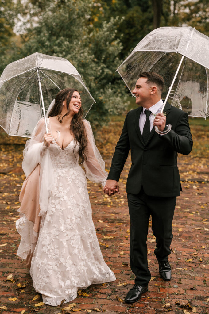 bride and groom holding hands and clear umbrellas during rainy wedding day at waterloo village nj 