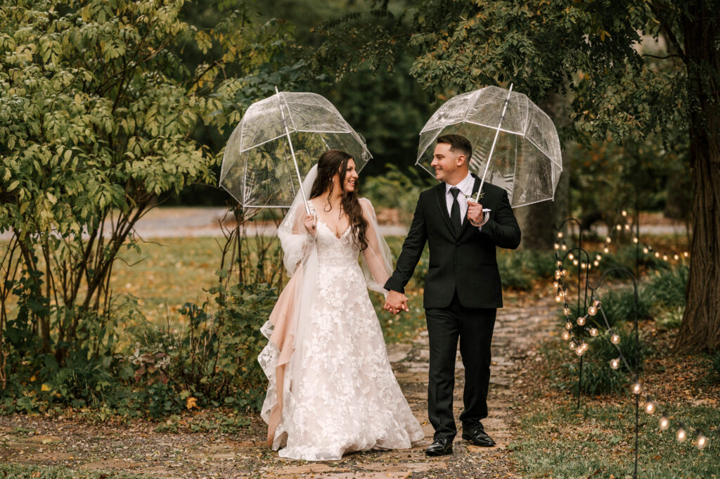 bride and groom holding clear umbrellas on stone path 
