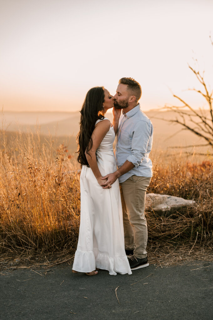 couple sharing a kiss in front of a field at bear mountain state park in ny