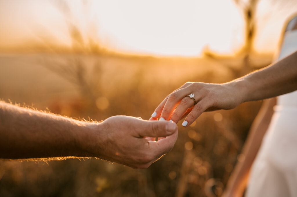 close up of hands touching and engagement ring with golden hour lighting behind them during engagement session in new york