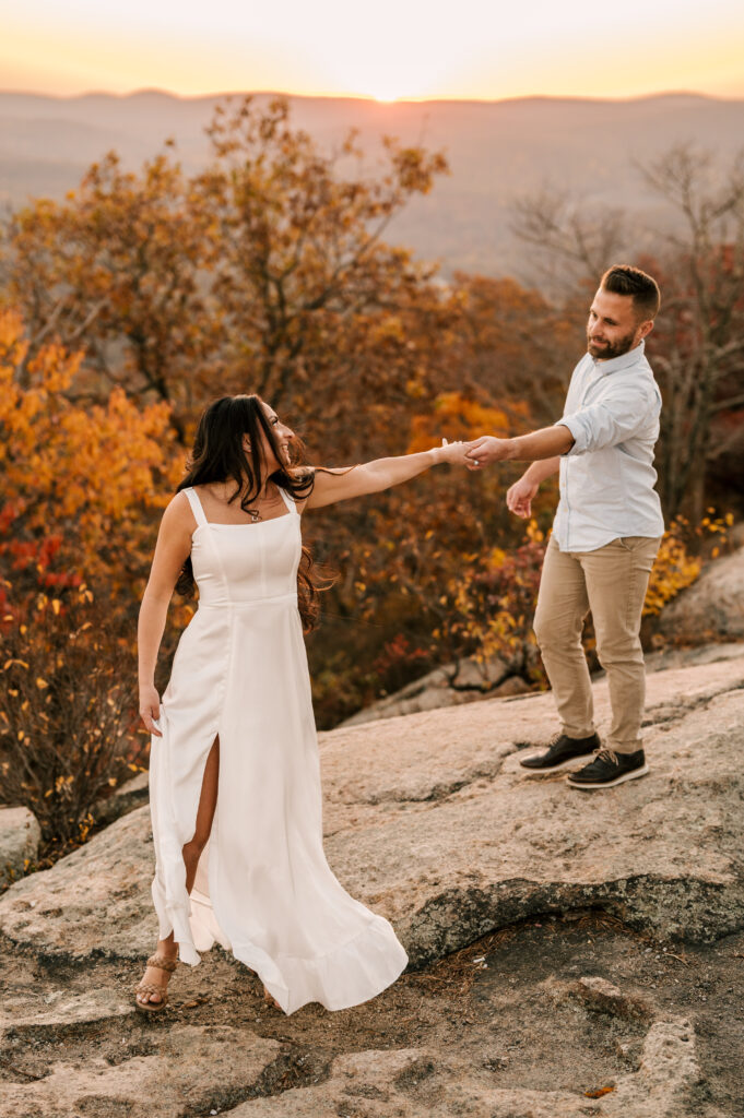 bride to be and fiance dancing on top of bear mountain state park overlooking the fall foliage engagement session