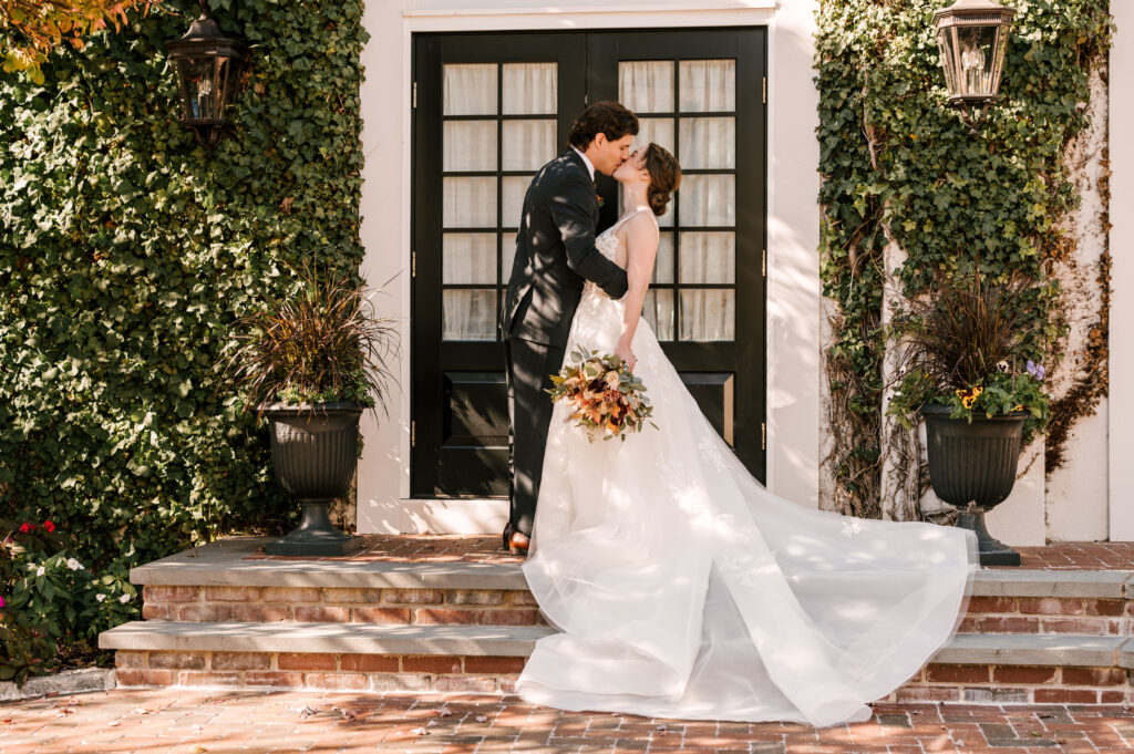 bride and groom kissing in front of french doors and greenery at david's country inn for their fall nj wedding