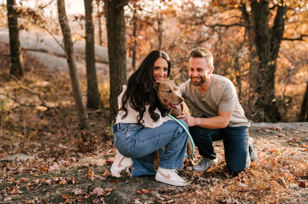 engaged couple and their dog in the fall foliage at bear mountain state park for engagement session