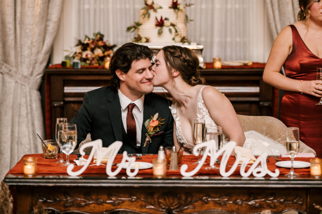bride kissing the groom's cheek at their sweetheart table during nj wedding in october