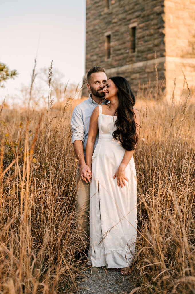bride to be wearing a white dress and smiling at her fiance in fall foliage during engagement session