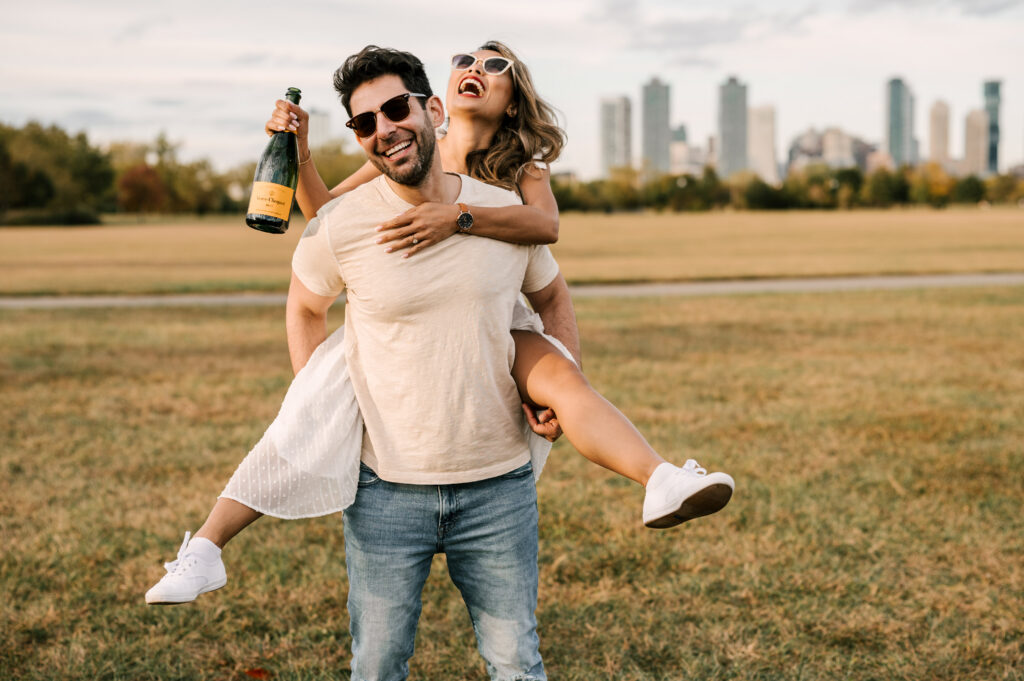 couple laughing with city skyline in the background during fall engagement shoot at liberty state park