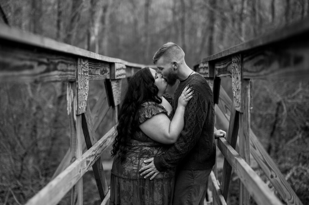 black and white shot of couple kissing on old wooden bridge during november engagement session