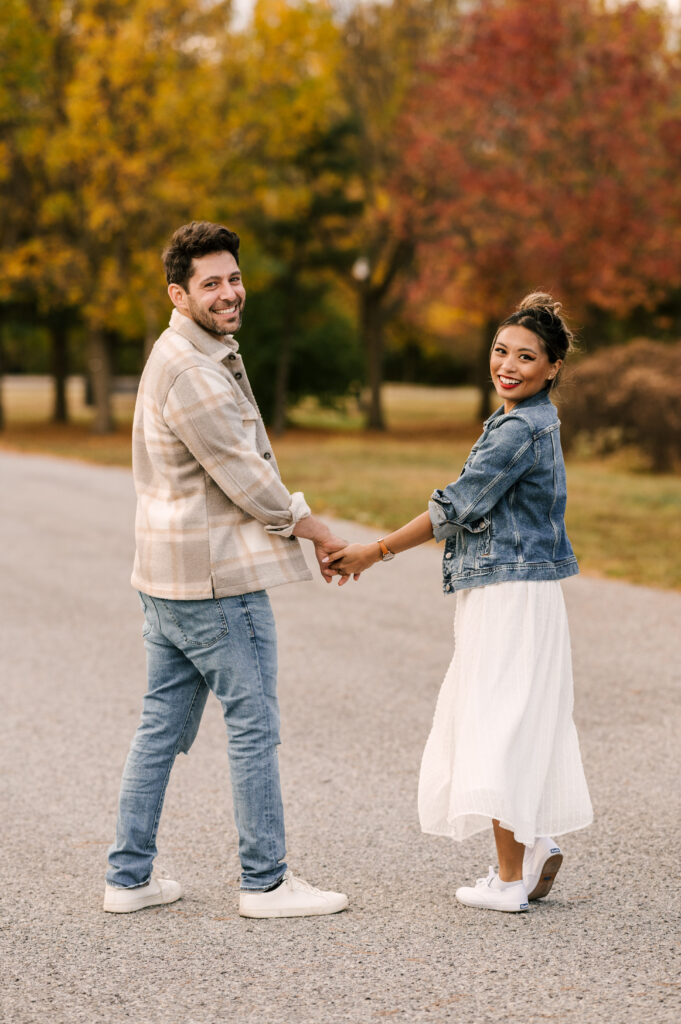 couple holding hands and smiling on path at liberty state park during engagement session