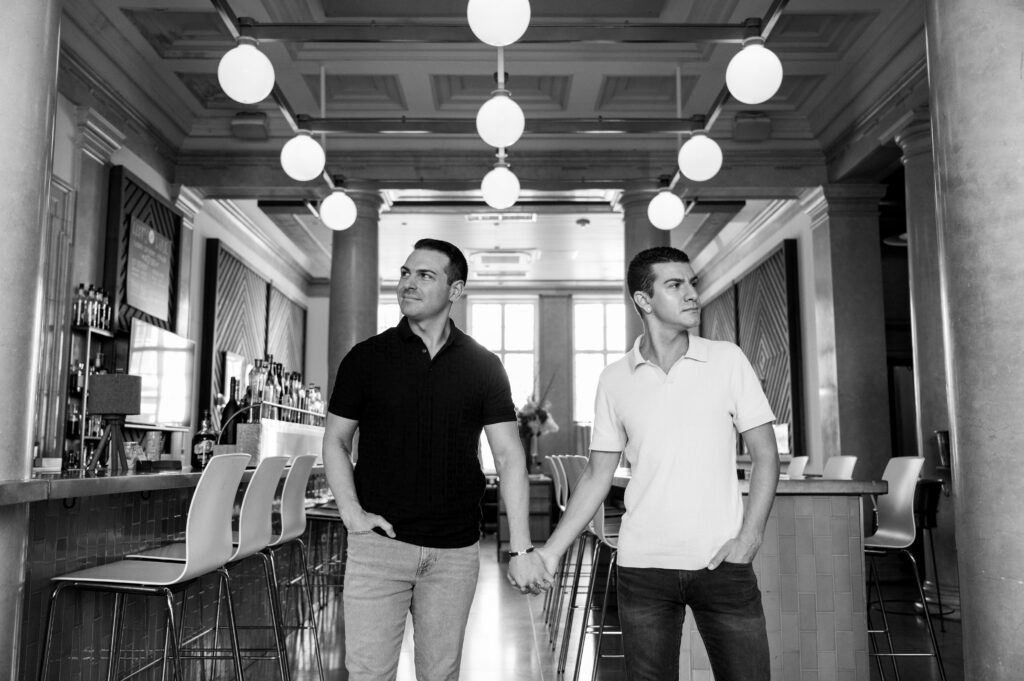 black and white image of couple holding hands with bar setting behind them during engagement shoot in new jersey