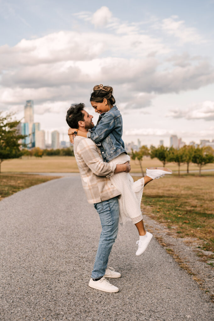 man lifting woman up with nyc skyline in the background at liberty state park october engagement session