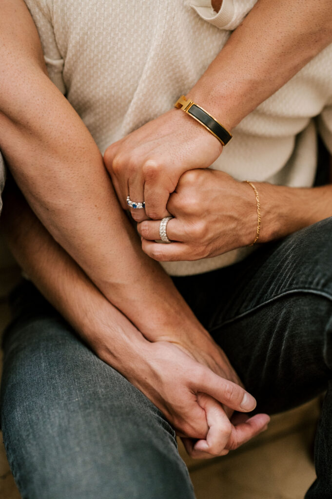 detailed close up of engagement rings, hermes bracelet and gold chain bracelet with couple's hands intertwined
