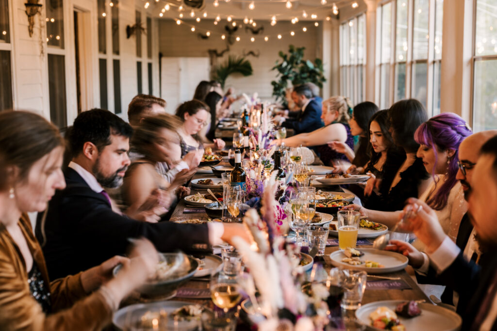intimate dinner table setting for april wedding in new york, guests all at one long table sharing a meal amongst pops of purples and pinks