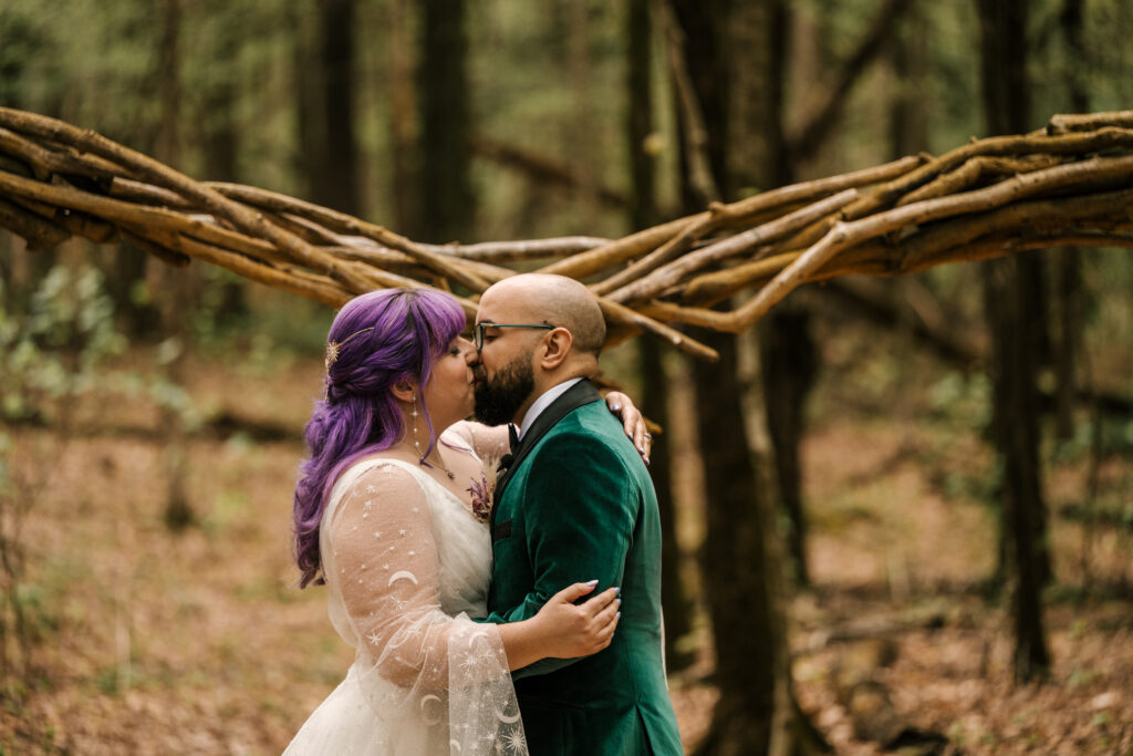 bride and groom sharing first kiss in wooded ceremony location at their april wedding