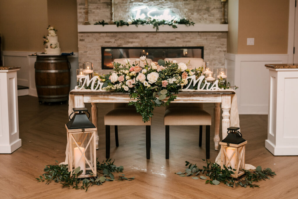 detail shot of bride & groom's sweetheart table with rustic lanterns, greenery, white & pink florals and a wooden Mr & Mrs sign