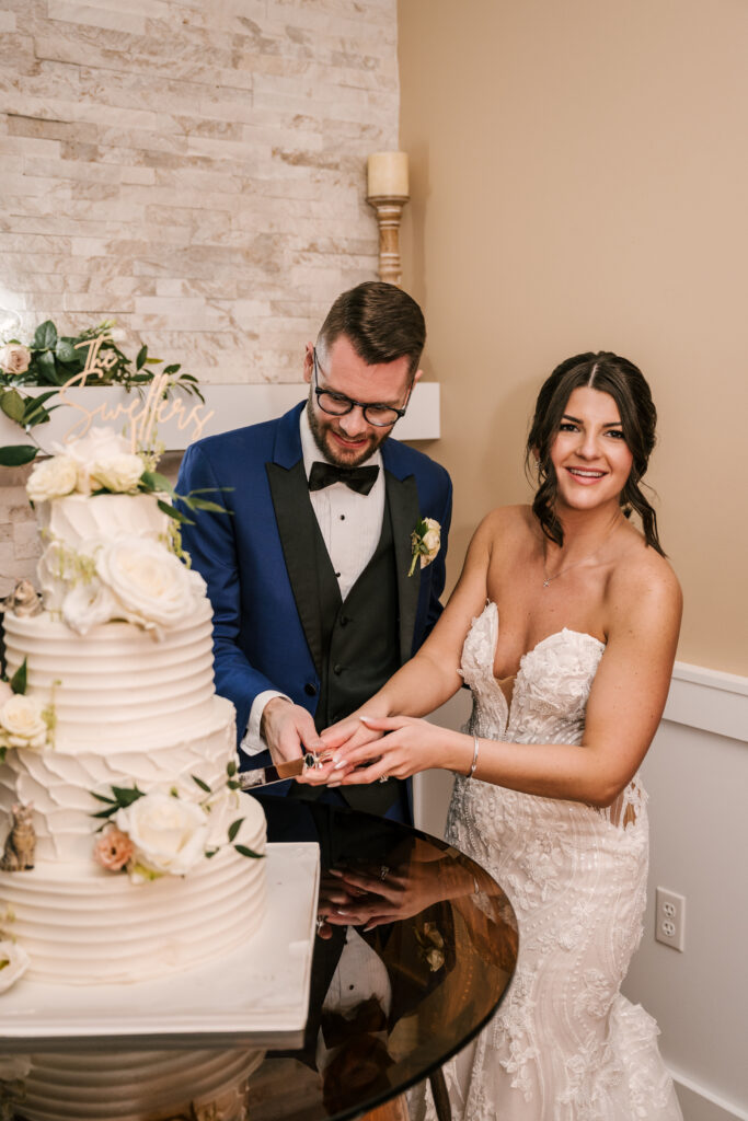 bride and groom cutting their wedding cake, detailed with white and pink florals and a script, gold cake topper