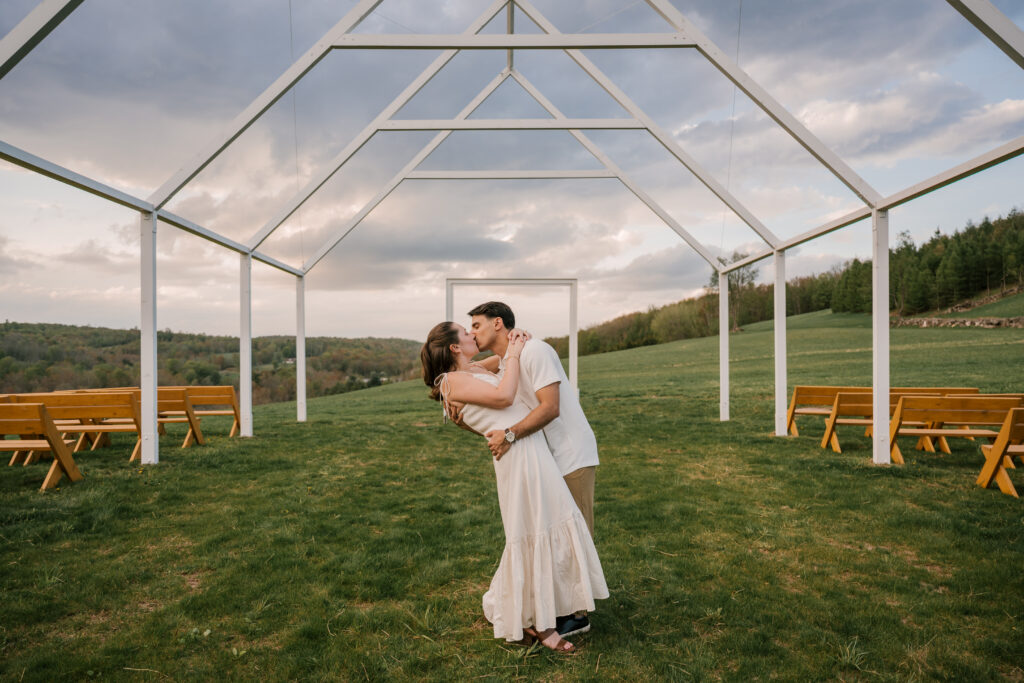 girl in white dress and brown heels and man in white t shirt and khaki pants kissing in a field